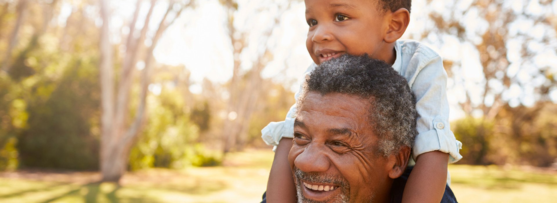 Grandfather Carries Grandson On Shoulders During Walk In Park